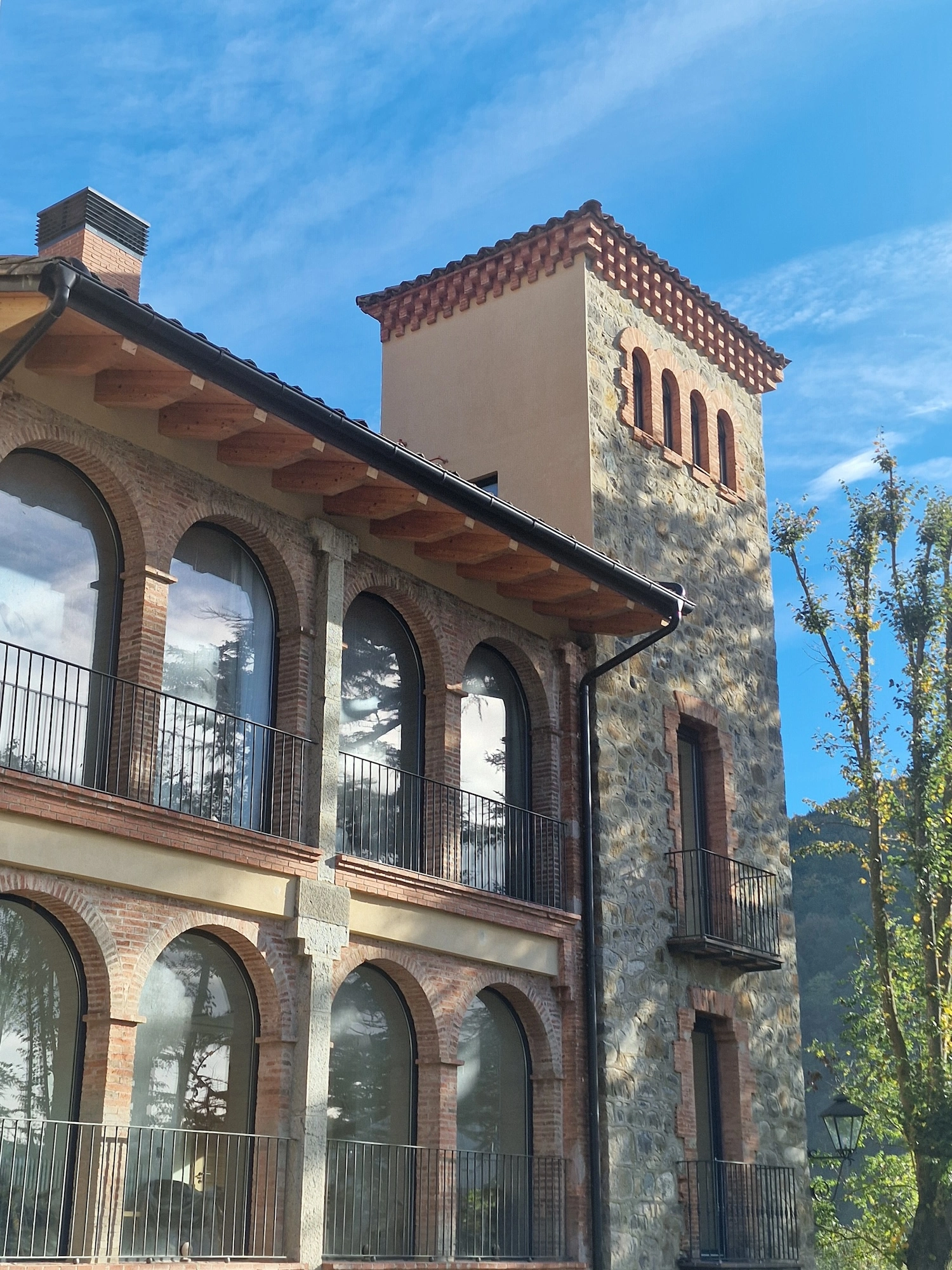 Façana principal amb grans finestrals d'arc i torre de la masia modernista Mas Pairó a Camprodon